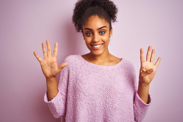 Young african american woman wearing winter sweater standing over isolated pink background showing and pointing up with fingers number nine while smiling confident and happy.