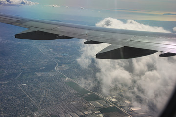 Looking out the window of a passenger jet at the wing and the ground below. Close up view of white clouds and blue skies.