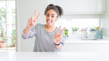 Beautiful african american woman with afro hair wearing casual striped sweater smiling with tongue out showing fingers of both hands doing victory sign. Number two.
