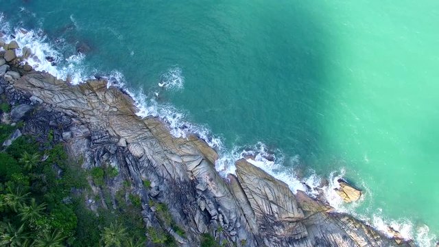 drone hovering above the diagonal line seashore coastline in Thailand turquoise water breaking of the rocks near palm trees moving sun shadow slow approximation to the water beautiful aerial landscape