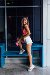 Stylish happy young brunette woman wearing white shorts and sneakers holding pink cup of coffee to go.