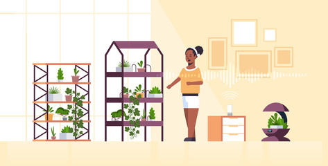 african american woman using automatic watering system controlled by smart speaker voice recognition activated assistant concept modern smart home garden interior flat full length horizontal