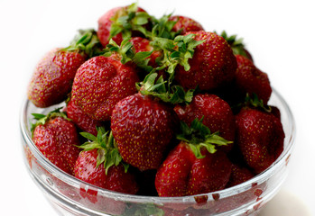 many sweet strawberries in a transparent plate on a white background