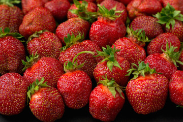 many sweet strawberries lies on a black background