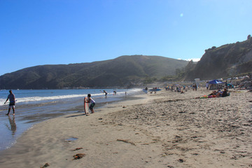 Crowds playiing on the beach. Mountains in the background with clear blue skies.