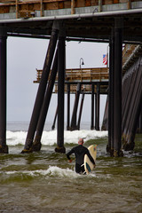 Surfer running into the ocean to catch the waves along side the pier.