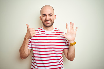Naklejka premium Young bald man with beard wearing casual striped red t-shirt over white isolated background showing and pointing up with fingers number six while smiling confident and happy.