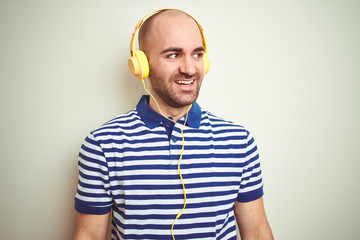 Young man listening to music wearing yellow headphones over isolated background looking away to side with smile on face, natural expression. Laughing confident.