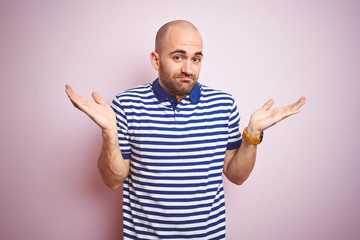 Young bald man with beard wearing casual striped blue t-shirt over pink isolated background...