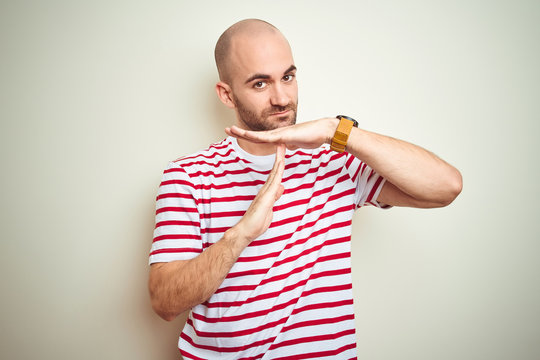 Young bald man with beard wearing casual striped red t-shirt over white isolated background Doing time out gesture with hands, frustrated and serious face