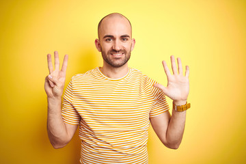 Naklejka premium Young bald man with beard wearing casual striped t-shirt over yellow isolated background showing and pointing up with fingers number eight while smiling confident and happy.