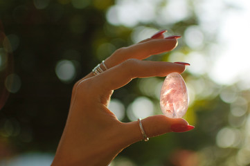Close up photo of female hand with transparent amethyst yoni egg for vumbuilding. Quartz crystal egg in hands on sunset background. Womens health concept