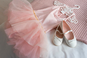 Little shoes and pink dress on a bed in kid bedroom. kid prepare to party. 