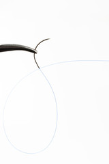 Needle holder with curved needle with blue thread.