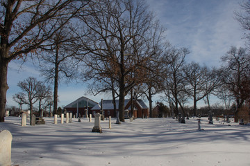 Snow covered cemetary. ormant trees, blue skies, with white clouds.