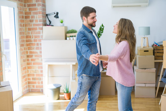Young couple dancing celebrating moving to new apartment around cardboard boxes
