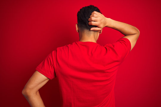 Young brazilian man wearing t-shirt standing over isolated red background Backwards thinking about doubt with hand on head