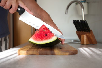 Closeup of woman's hand cutting watermelon on wooden cutting board in the kitchen