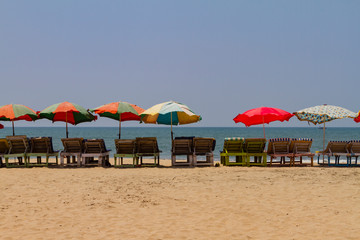 Row of covered wooden deck chairs with colorful umbrellas on the beach in GOA, India. Sea summer background. Holiday template.