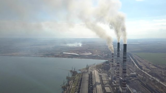 Aerial view of high chimney pipes with grey smoke from coal power plant. Production of electricity with fossil fuel.