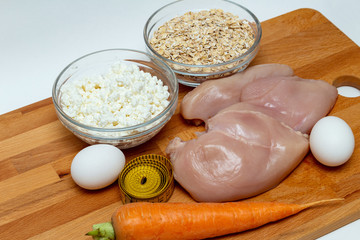 raw chicken breast, cereals, eggs, measuring tape, farm cottage cheese carrot close up on wooden background protein healthy diet fat free concept eco product sports nutrition