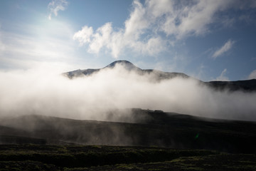 Misty magical morning in Avacha base camp. Kamchatka Peninsula, Russian far east. Mountain peaks and ribs of the volcano. Clouds creating mystical landscape. Direct sun through veil of fog