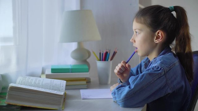little school girl chewing pen and counting on fingers while doing her homework