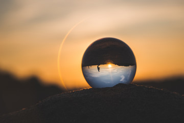 in a crystal ball lying on the sand, people and the setting sun are reflected