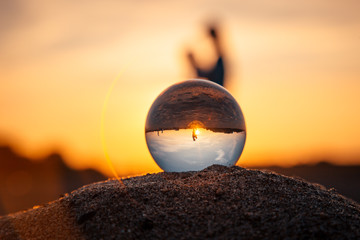 in a crystal ball lying on the sand, people and the setting sun are reflected