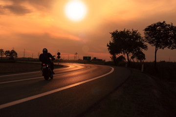 Motocyklista na tle zachodzącego słońca, droga szybkiego ruchu. - obrazy, fototapety, plakaty