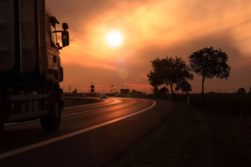 Samochód ciężarowy, tir na tle zachodzącego słońca, droga szybkiego ruchu.	