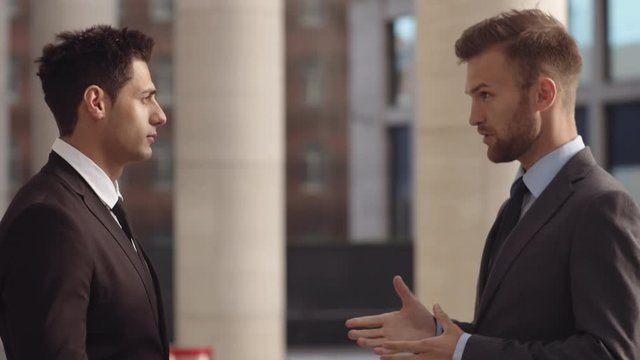 Medium shot of two young multiethnic businessmen standing in front of each other outside and having business talk