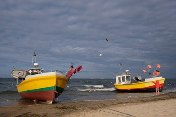 Two wooden fishing boats on the beach of Baltic Sea in Sopot/Poland. Silhouette of little boy in red jacket standing near boat and pointing his hand at flying seagulls.