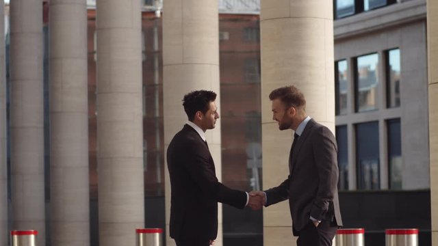 Medium shot of two diverse male business partners going towards each other and shaking hands