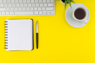 Flat lay view of office table desk. Workspace with keyboard, pen, book, coffee and decoration flower on yellow background. Copy Space concept