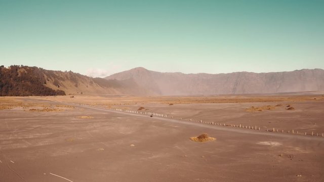 Cinematic shot aerial drone view of motorbike rider driving in a volcanic dusty desert near beautiful Mount Bromo in East Java, Indonesia
