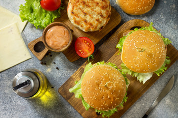 Delicious grilled burgers, hamburger sandwich with cutlet of chicken meat, melted cheese, tomatoes and bacon on a wooden board. Top view flat lay.