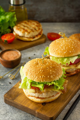 Delicious grilled burgers, hamburger sandwich with cutlet of chicken meat, melted cheese, tomatoes and bacon on a wooden board.