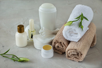 Close up of the set for body care: a few rolled towels, antiperspirant, cotton pads, cotton buds, bottle of lotion, balsam for lips, nail polish with eustoma on the white background