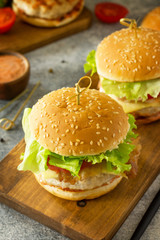 Two homemade burgers with cutlet of chicken meat, melted cheese, tomatoes and bacon on a wooden board.