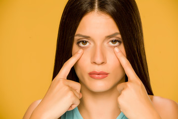 Young woman touching her  low eyelids on yellow background