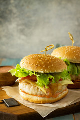 Two homemade burgers with cutlet of chicken meat, melted cheese, tomatoes and bacon on a wooden board. Free space for your text.