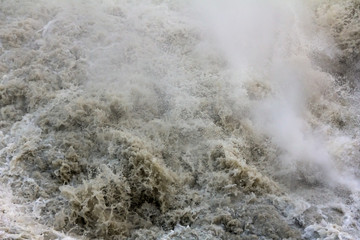 Raging water in a muddy mountain river after a waterfall