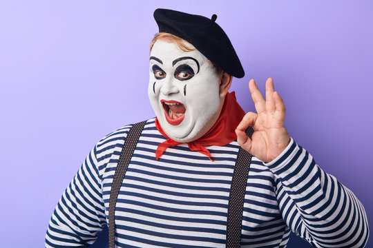 plump clown showing OK sign, making funny grimaces and showing exaggerated gestures Studio shot, blue background.feeling and emotion.