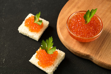 Delicious red caviar on wheat bread served with parseley on wooden desk.
