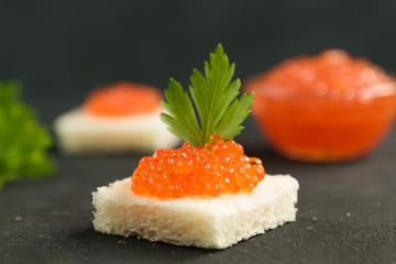Square shaped sandwich with red caviar on black background
