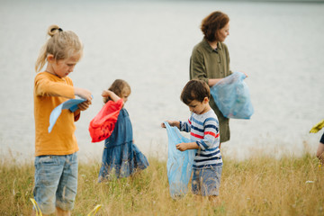 Fototapeta premium Mother with her kids collecting garbage on a meadow next to the river 