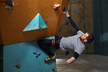 Side view of motivated strong rock-climber with physical disability, training at colourful...
