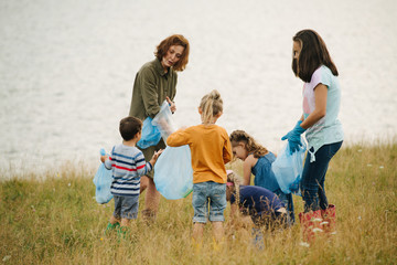 Woman with group of kids collecting garbage on a meadow next to the river