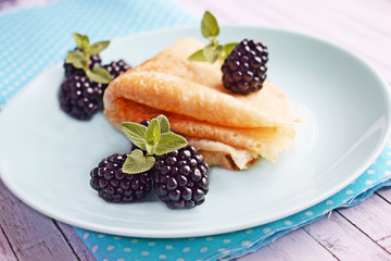 Delicious hot pancakes with blackberries and mint on a wooden background.